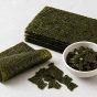 Sheets and strips of raw nori seaweed arranged on a light tabletop beside a small bowl.